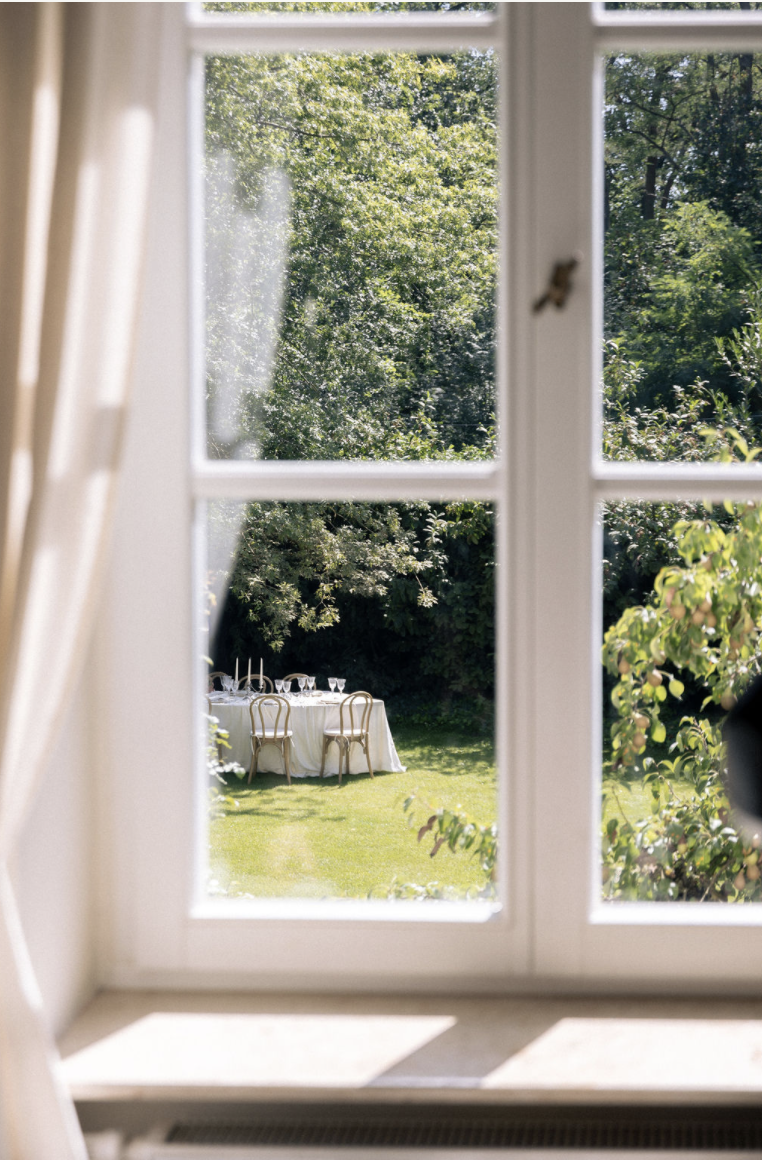 Blick durch ein helles Fenster auf eine Hochzeitstafel im Garten