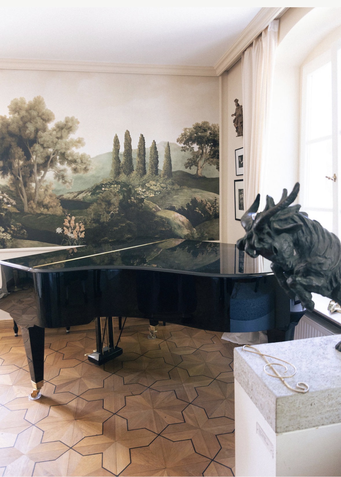 Glänzender schwarzer Konzertflügel in einem Salon mit historischer Landschaftstapete und Sternparkett