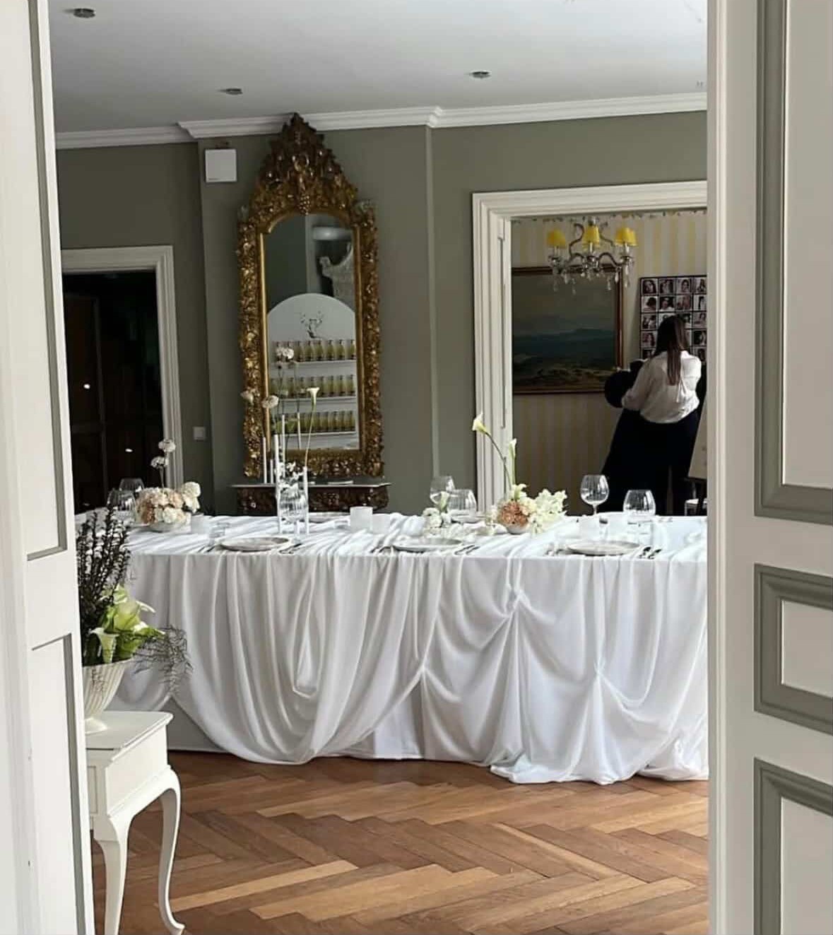Blick durch eine weiße Flügeltür auf eine lange Festtafel mit weißer Tischdecke, Kerzen und Blumen