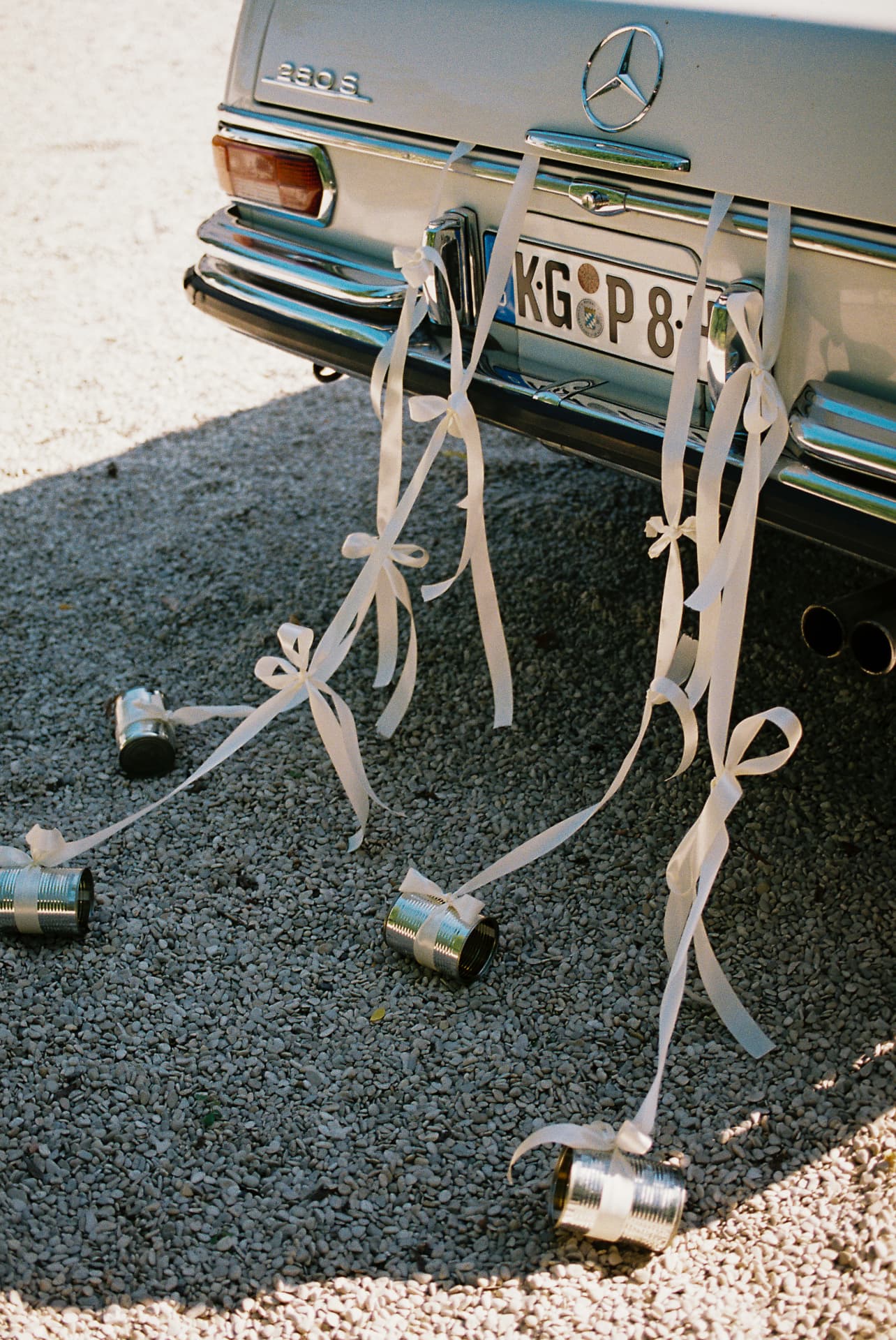 Ein oldtimer auf einem Kiesweg, an dessen Heck weiße Schleifen und Blechdosen befestigt sind