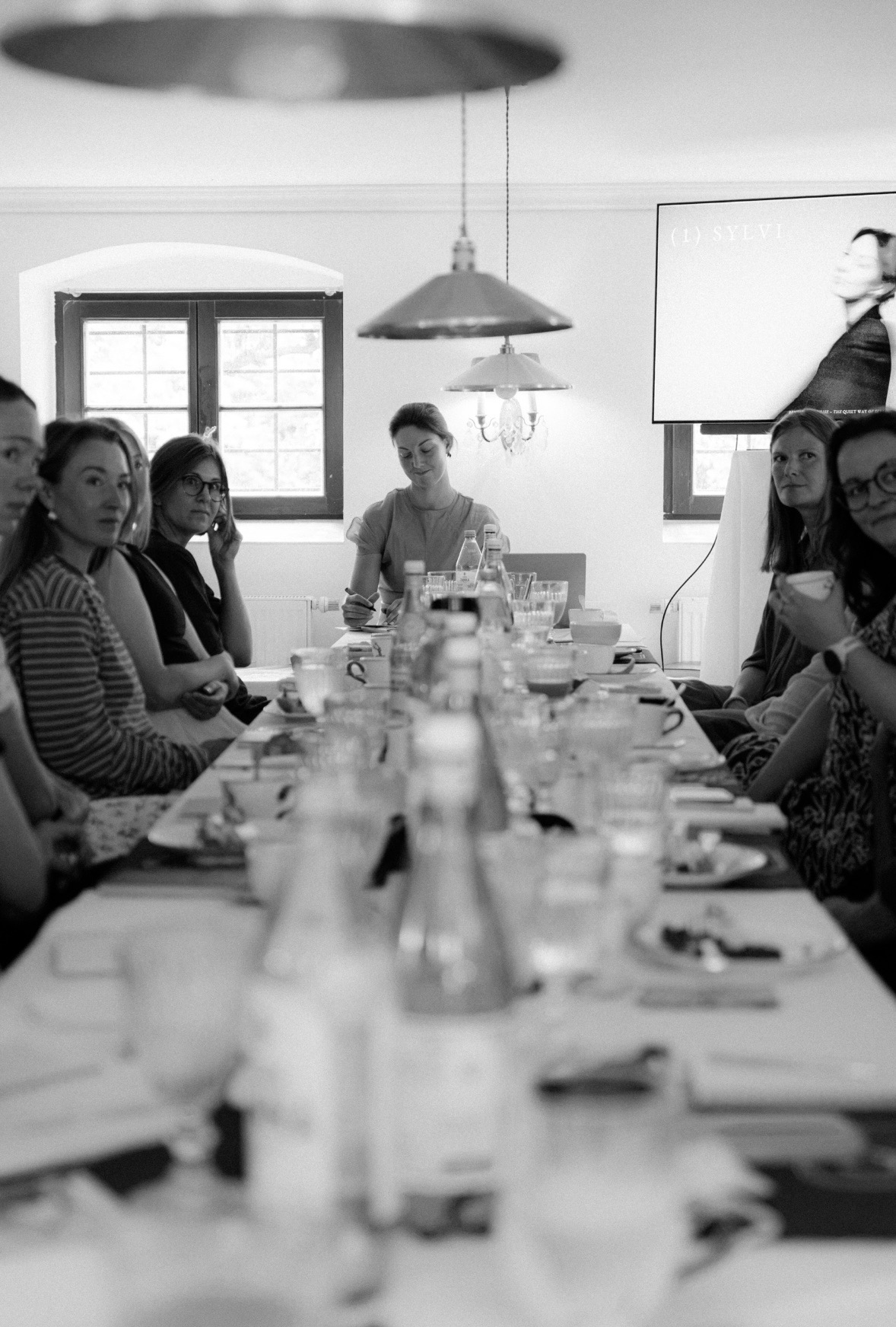 Workshopteilnehmer:innen im Gespräch am gemeinsamen Tisch in der Villa Fuchs, fotografiert in Schwarz-Weiß